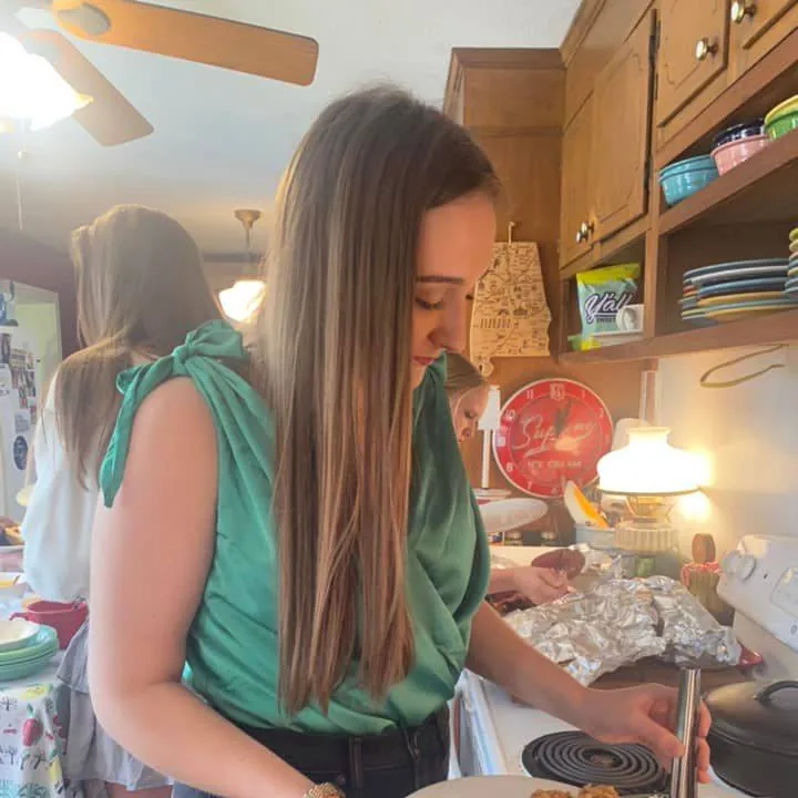 A young woman working carefully at the stove while other family members prepare food nearby