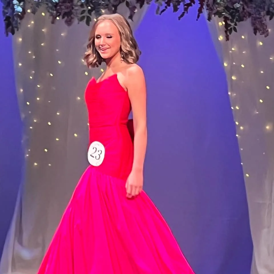 A young woman in a vivid pink gown walking beneath stage lights